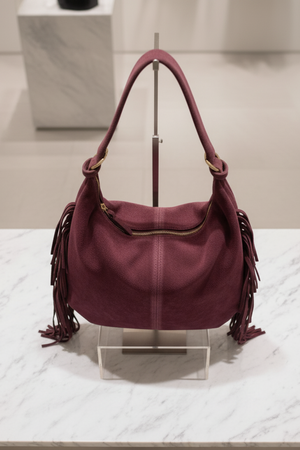 Borsa con frange laterali in camoscio bordeaux RAELA esposta su piano in marmo